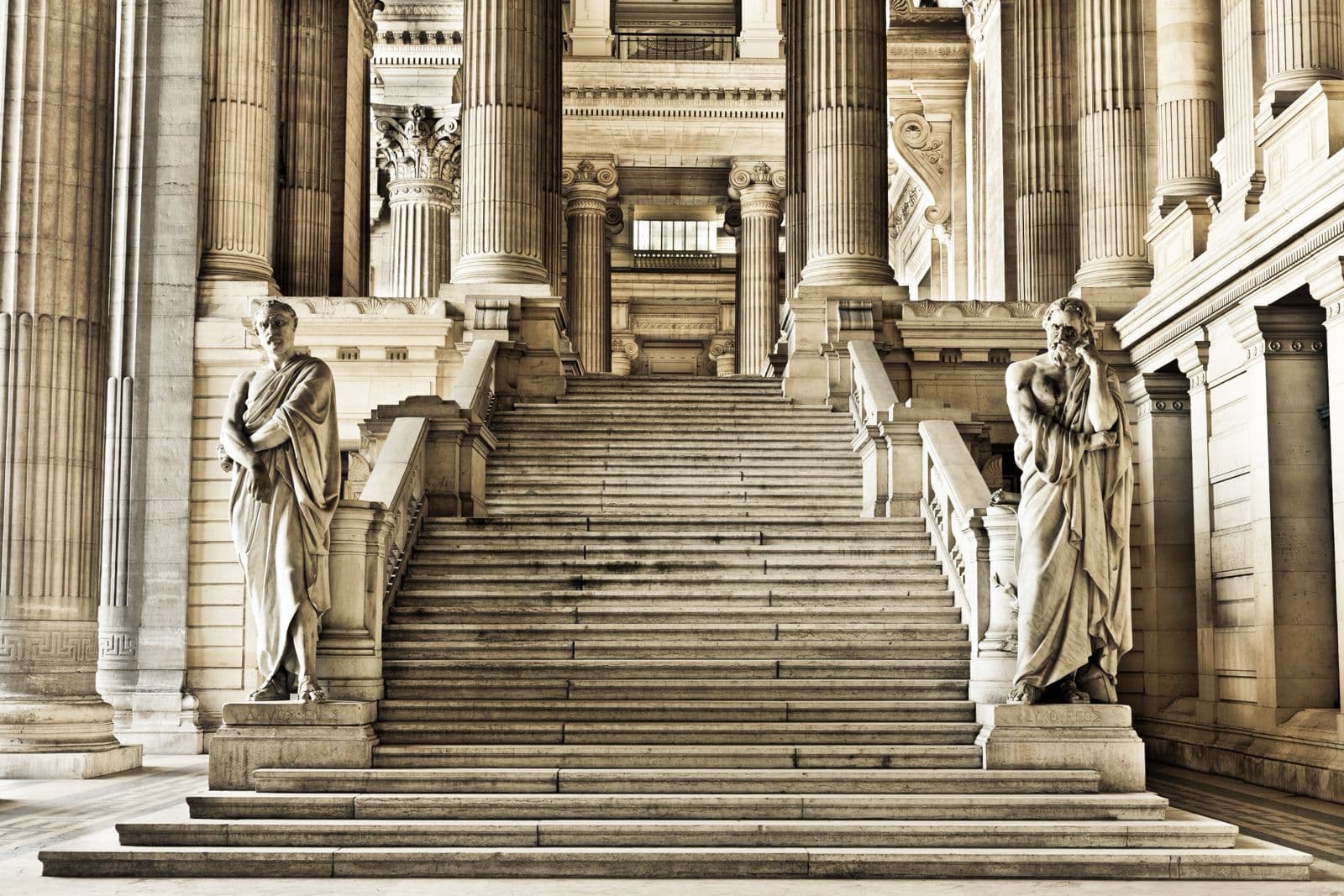 Escalier monumental d’un palais de justice, bordé de colonnes et de statues antiques.